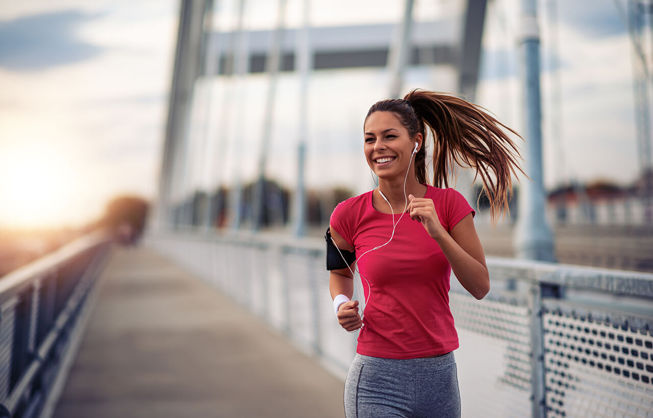 Mulher jovem feliz com fone de ouvido enquanto pratica corrida ao ar livre em uma ponte