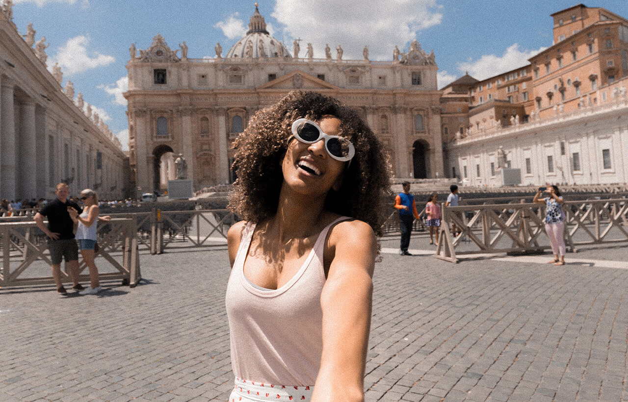 Mulher sorrindo enquanto tira selfie em frente à Basílica de São Pedro no Vaticano