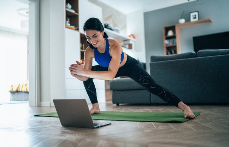 Mulher feliz fazendo alongamento em casa em frente ao computador em tapete de yoga