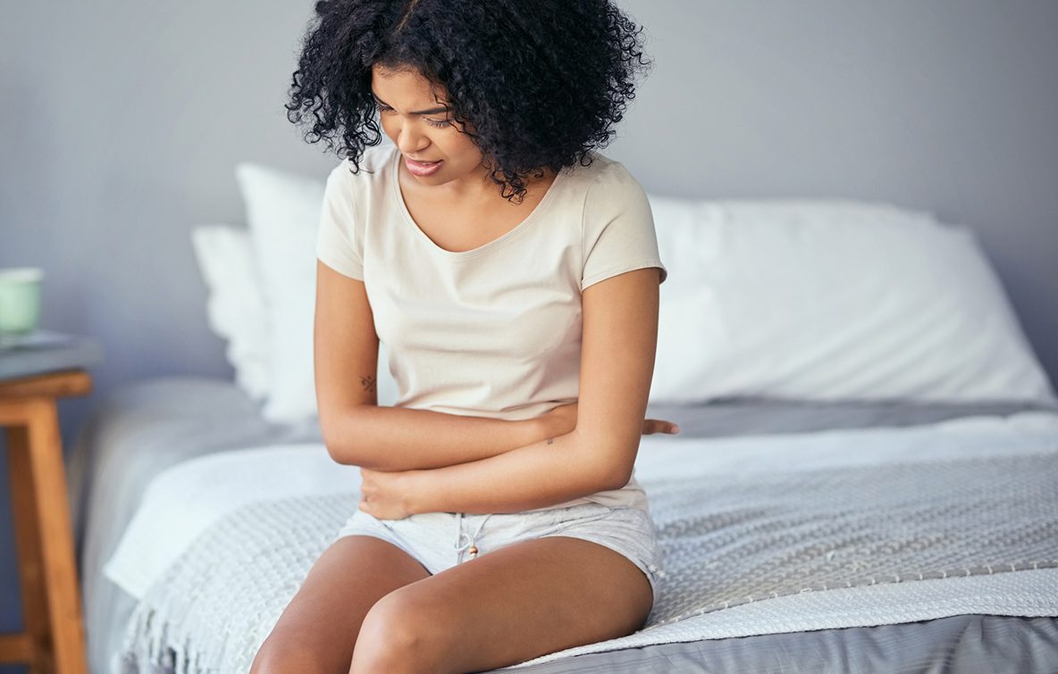 Mulher negra e jovem com dor sentada na cama