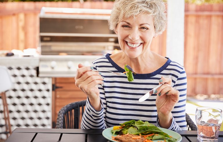 Idosa feliz em comer salada com grelhado: comida saudável na terceira idade