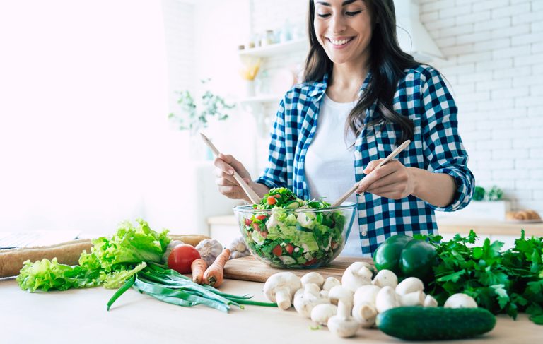 Mulher feliz preparando salada em tigela com alimentos saudáveis: cogumelos e verduras